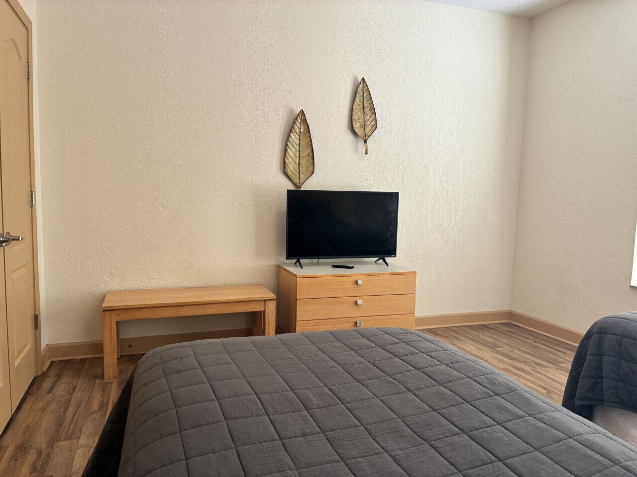 A bedroom with a bed, a wooden nightstand, a TV, and two decorative leaves on the wall.