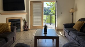 A living room with a fireplace, a flat-screen TV, two sofas, a coffee table, and a sliding glass door leading to a balcony. - Mountain View Zodiac - Unit 3201 - FREE Attraction Ticket with EACH night Stay Including Dollywood (Pigeon Forge)