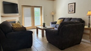 A living room with two dark sofas, a coffee table, a TV mounted on the wall, and a door with blinds. - Mountain View Zodiac - Unit 3201 - FREE Attraction Ticket with EACH night Stay Including Dollywood (Pigeon Forge)