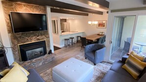 A modern living room with a fireplace, a flat-screen TV, and a dining area with bar stools.