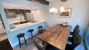A modern kitchen with stainless steel appliances, a light blue island with bar stools, and a dining area with a wooden table and chairs.