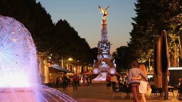 Een fontein met een standbeeld in het midden, omringd door bomen en mensen die lopen.