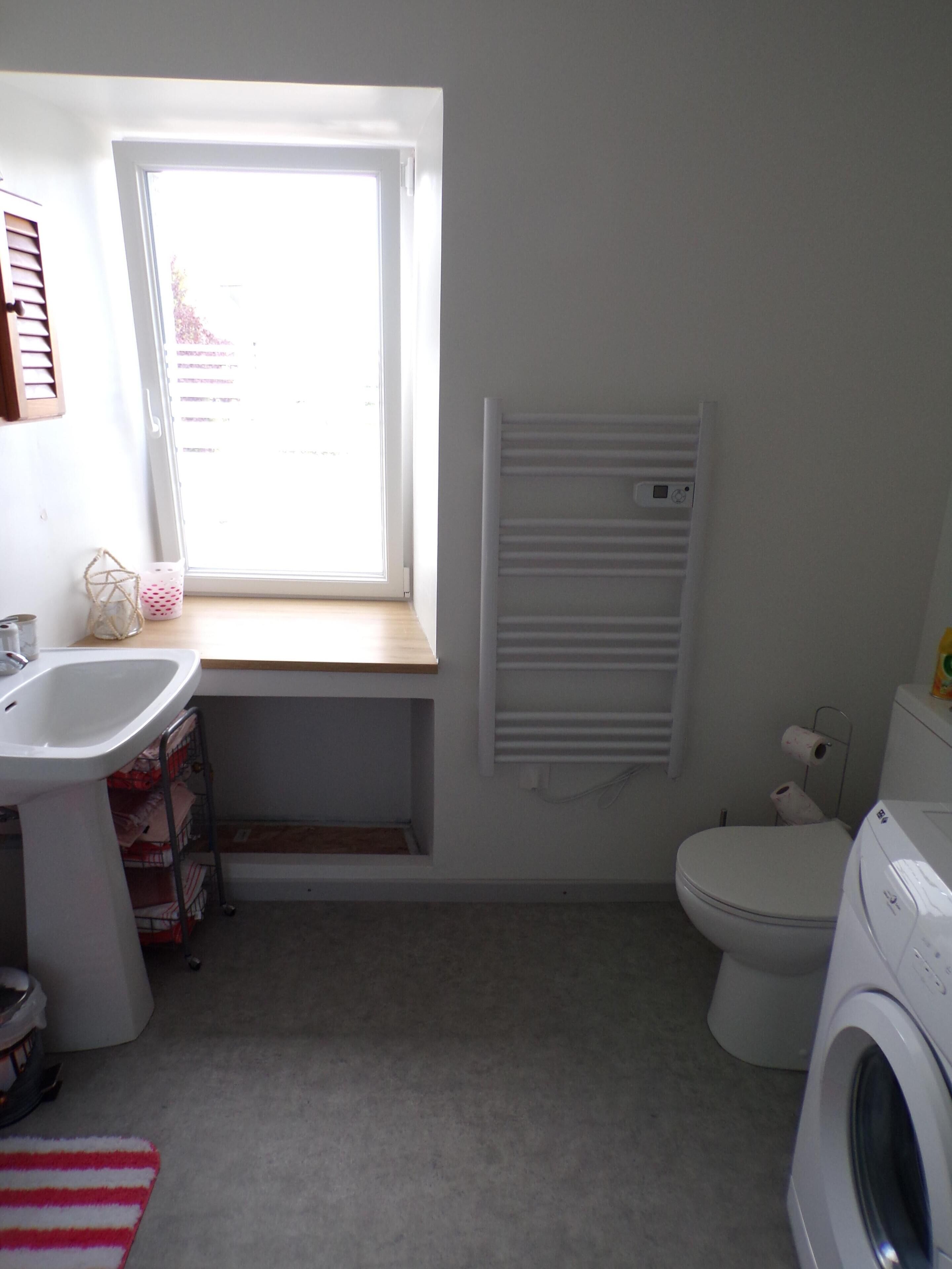 A compact bathroom with a window, a sink, a toilet, and a washing machine.
