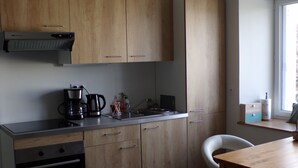 A compact kitchen with wooden cabinets, a coffee maker, a kettle, and a small window. - Quiet studio near the sea (Binic)