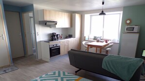 A compact living space with a kitchenette, a dining area, and a sofa with a blanket. - Quiet studio near the sea (Binic)