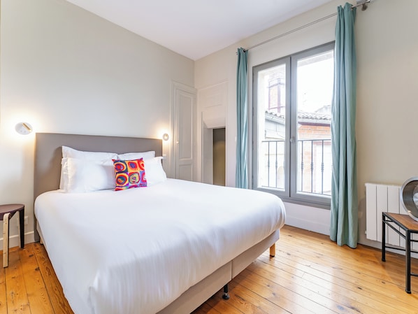 A hotel room with a large bed, a view of the outside, and a radiator on the wall.