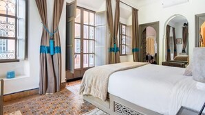 Een slaapkamer met een groot bed, gordijnen, een raam met uitzicht en een betegelde vloer.