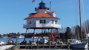 Una estructura de faro con un balcón, una bandera y un muelle con barcos.