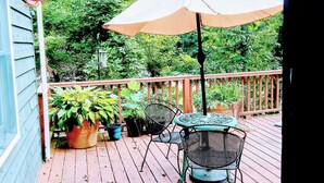 Una terraza de madera con una mesa y sillas, rodeada de plantas en macetas y un gran paraguas.