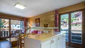 A cozy kitchen with wooden cabinets, a central island, and a view of a hotel sign outside. - Village Center, Near Ski Slopes, Courses, and Shops (La Clusaz)