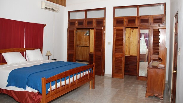A bedroom with a wooden bed, a red curtain, and a wooden wardrobe with glass doors. - Luxurious Rooms And Crisp, Virgin Mountain Air Awaits....Chef on Call (Cave Valley)
