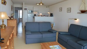 A living room with a sofa, a wooden coffee table, and a lamp. There is a kitchen area in the background with cabinets and a microwave.