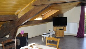 Een eetgedeelte met een tafel gedekt voor twee personen, een televisie op een meubel en een raam met gordijnen.