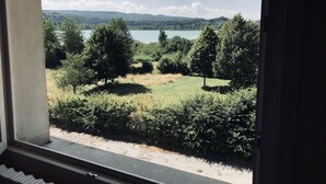 Uitzicht vanuit een raam op een meer, omringd door bomen en heuvels.