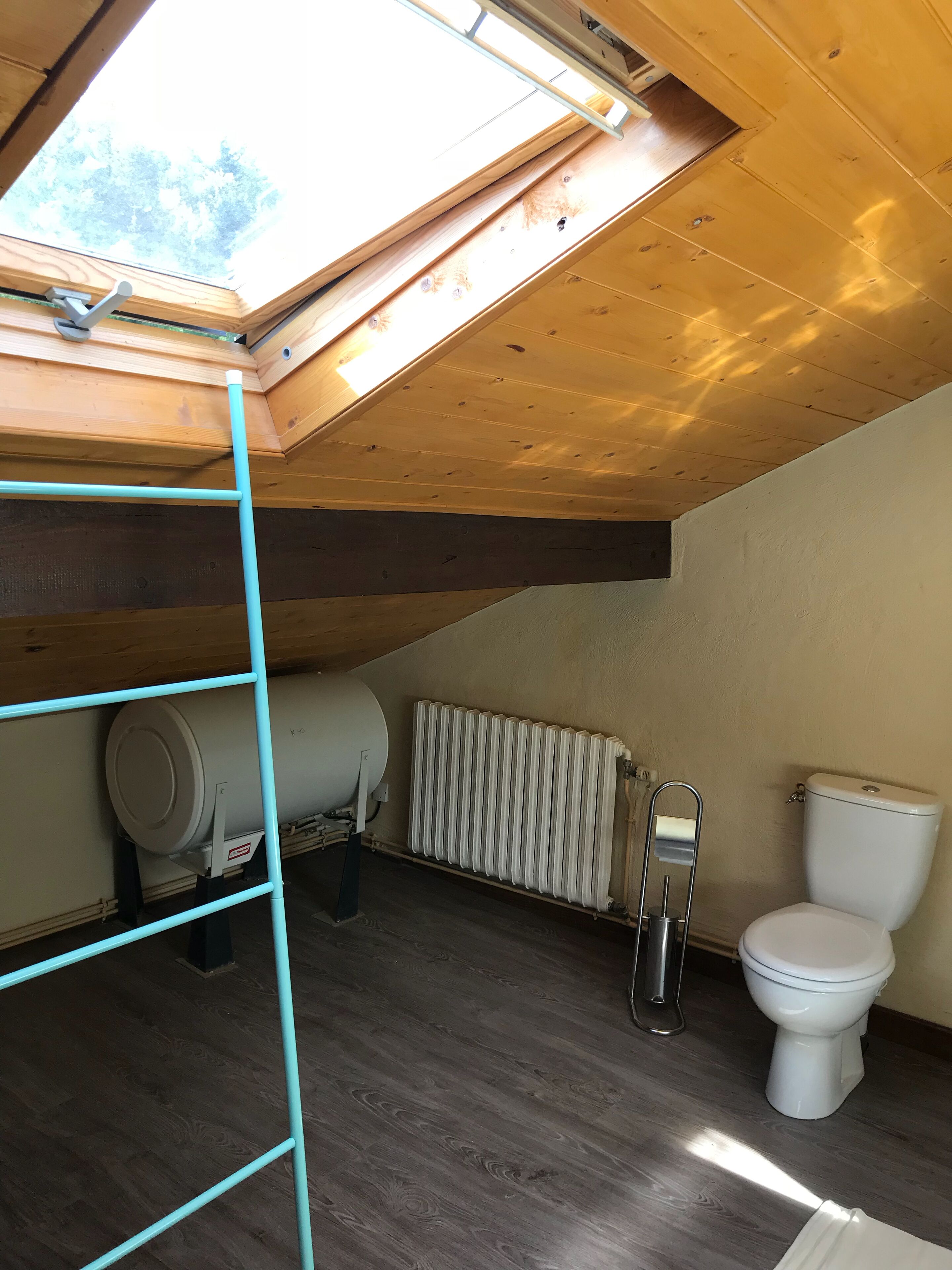 Un espacio ático pequeño y con una sola habitación, con tragaluz, radiador y un inodoro.
