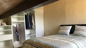 Een slaapkamer met een bed, een kledingkast en een plank met kleding en een hoed.