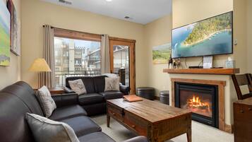 A living room with a sofa, coffee table, fireplace, television, and large windows.