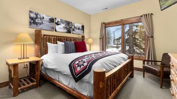A bedroom with a wooden bed, two bedside tables, a chair, and a large window with a view of trees.