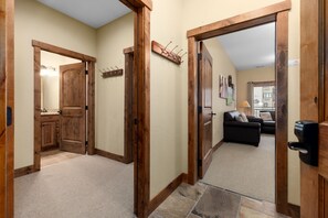 Un couloir avec des portes en bois, un porte-manteau et un coin salon comprenant un canapé et une lampe.