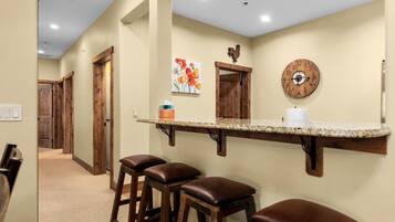 A hallway with wooden doors, a kitchen area with a bar counter, stools, and a clock on the wall.