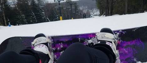 A snowboarder's feet on a purple snowboard with a snowy background and trees.