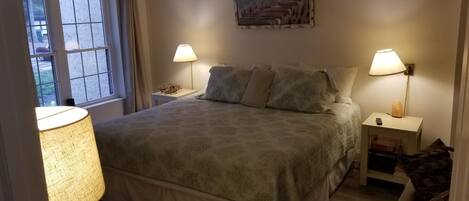 Un dormitorio con una cama, dos mesitas de noche, una lámpara y un cuadro en la pared.