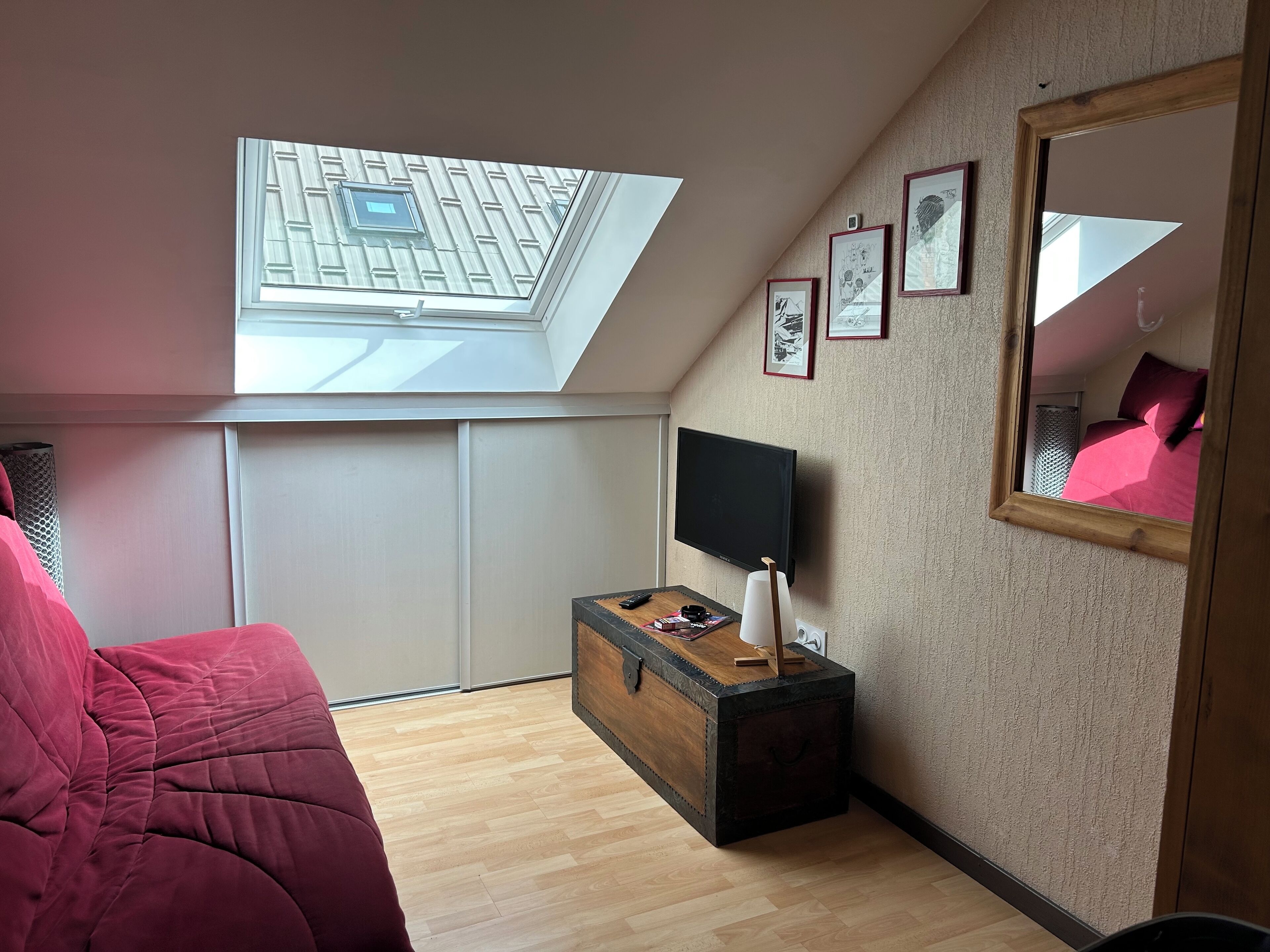 Una camera da letto con un lucernario, un letto, una TV, uno specchio e quadri appesi al muro.