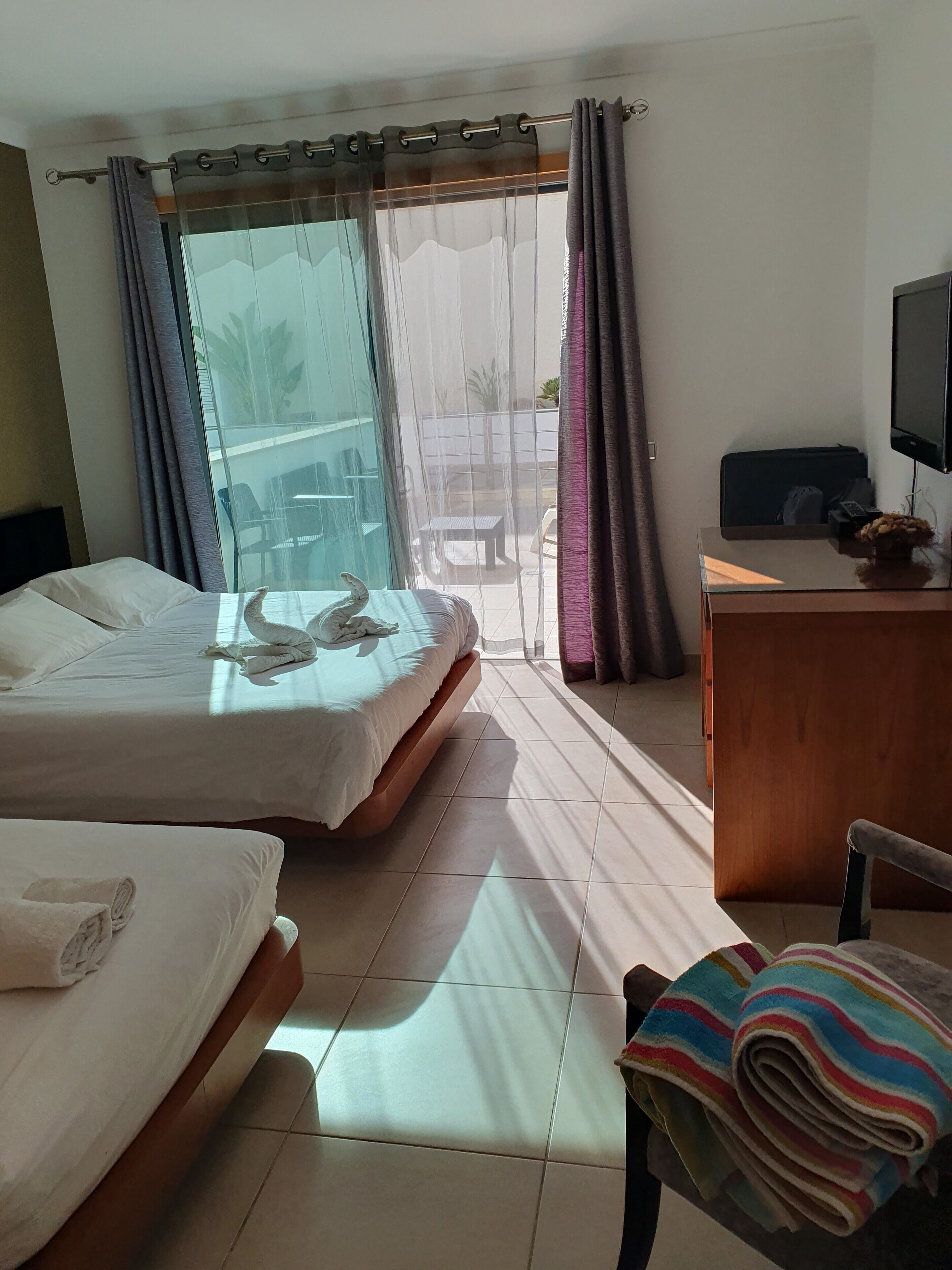 A hotel room with two beds, a desk with a TV, and a view of the outside.