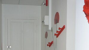 En hall med en vit dörr, en vit bänk och röda, blommiga dekorationer på väggen.