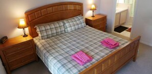 A neatly made bed with a plaid bedspread, two pillows, and two pink towels folded on the bed. There are two bedside tables with lamps, and a wooden headboard. - Ly217376 - Oak Island Cove - 4 Bed 3 Baths Villa (Kissimmee)