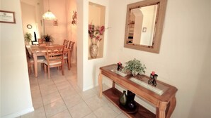 A dining area with a wooden table and chairs, a console table with decorative items, and a mirror on the wall. - Ly217376 - Oak Island Cove - 4 Bed 3 Baths Villa (Kissimmee)