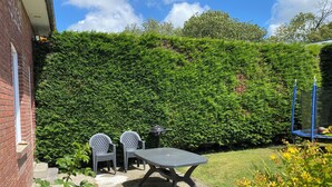 Un patio con una mesa, sillas, un muro de ladrillo y un seto verde.