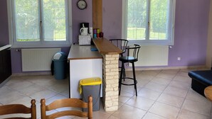 Cocina con una isla de piedra, dos sillas negras, una silla de madera, un cubo de basura y un reloj en la pared.