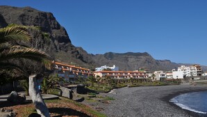 A coastal hotel with multiple buildings, a rocky beach, and a mountain in the background. - New 2010 - 1 bdrm penthouse, ocean front, south and north facing terrace, luxury (Garachico)