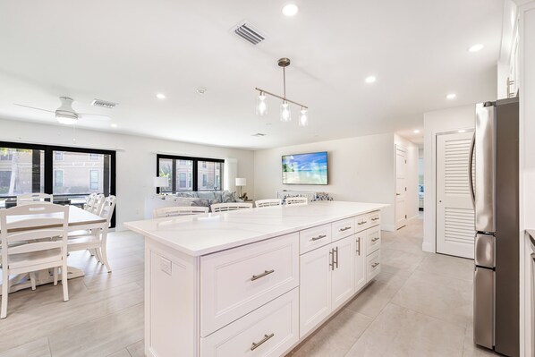 A modern kitchen with white cabinetry, a large island, and a stainless steel refrigerator.