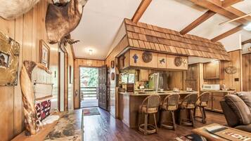 Interior rústico de una cabaña con paredes de madera, una zona de cocina y un comedor.