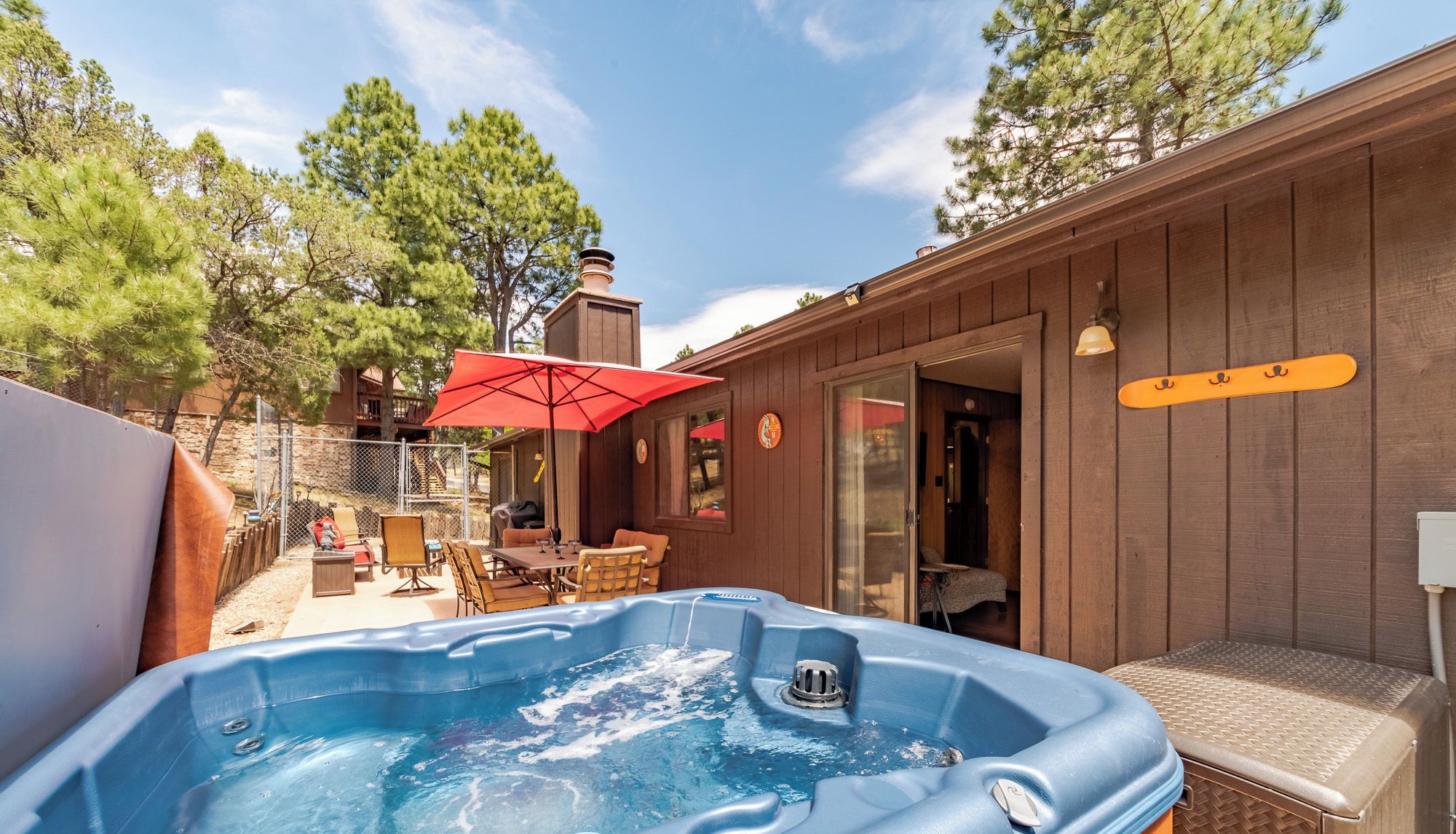Un jacuzzi con terraza de madera, un espacio de patio con mobiliario exterior, y una construcción de madera con chimenea.