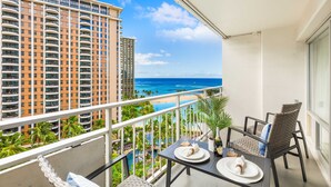 A balcony with a table set for two, overlooking a beach and a pool area with palm trees. - Ocean & Fireworks Views Condo at the Ilikai Hotel w/Full Kitchen & Free WiFi (Honolulu)