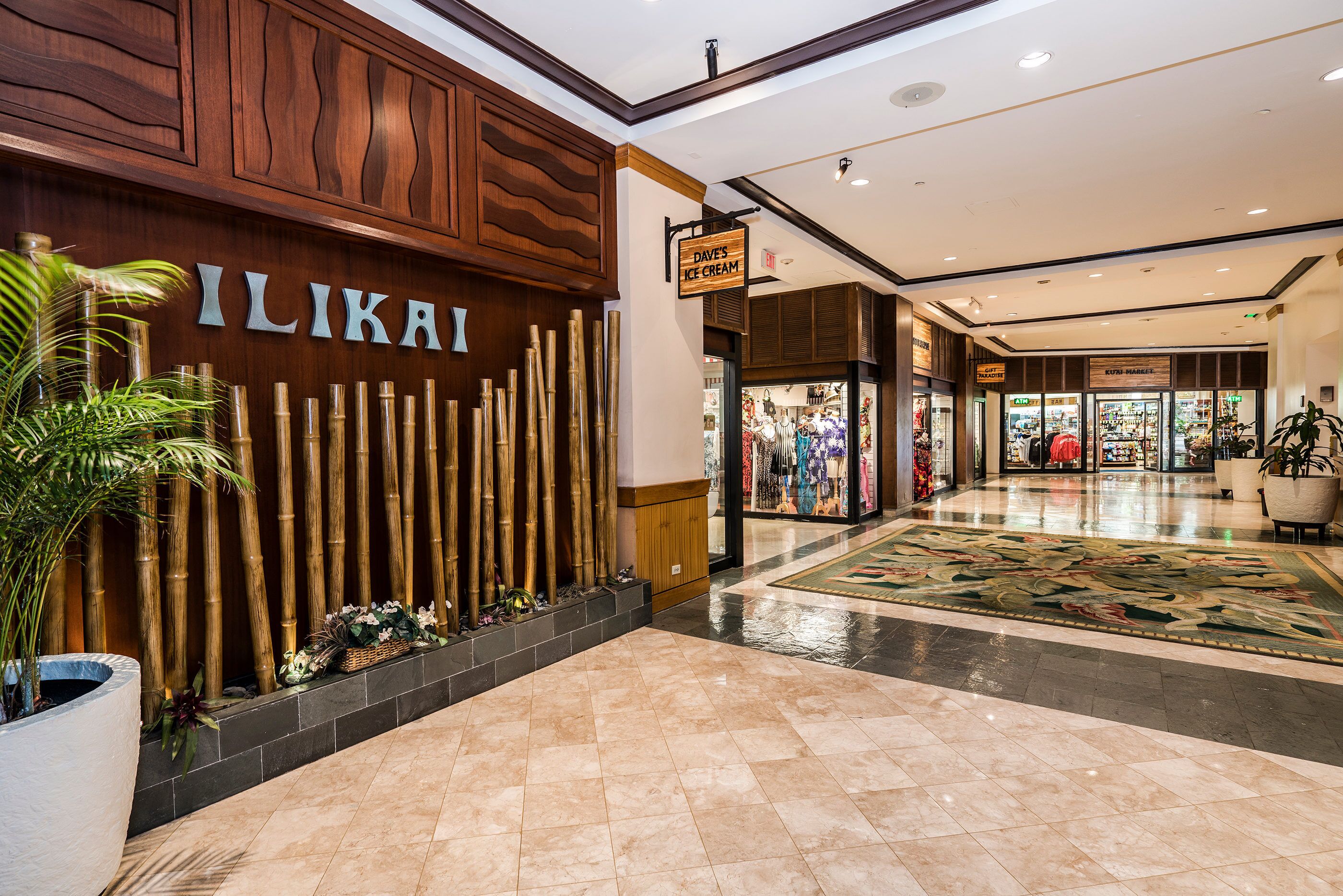 Interior d'un centre comercial amb un rètol de 'ILIKAI', una paret de bambú i una botiga de gelats 'DAVE'S ICE CREAM'.