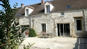 A stone building with a tiled roof, a patio with a table and chairs, and a small garden area. - Les Lattis: Cottage restored in the traditions, in a typical farm of Vexin (Avernes)
