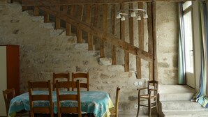 A rustic interior with a stone wall, wooden staircase, and a dining area with chairs and a table. - Les Lattis: Cottage restored in the traditions, in a typical farm of Vexin (Avernes)