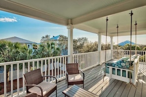A covered porch with wicker furniture, a swing, and a view of houses and trees.