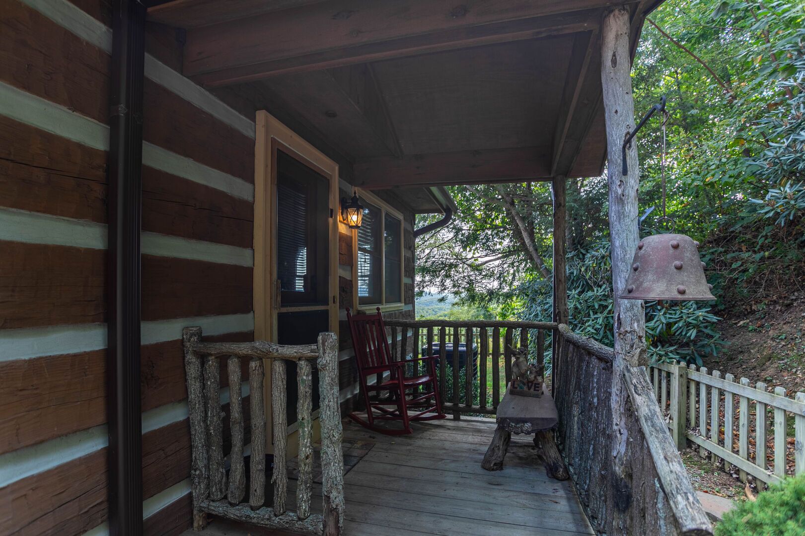 A wooden porch with a rustic design, featuring a wooden railing, a bench, and a red chair.