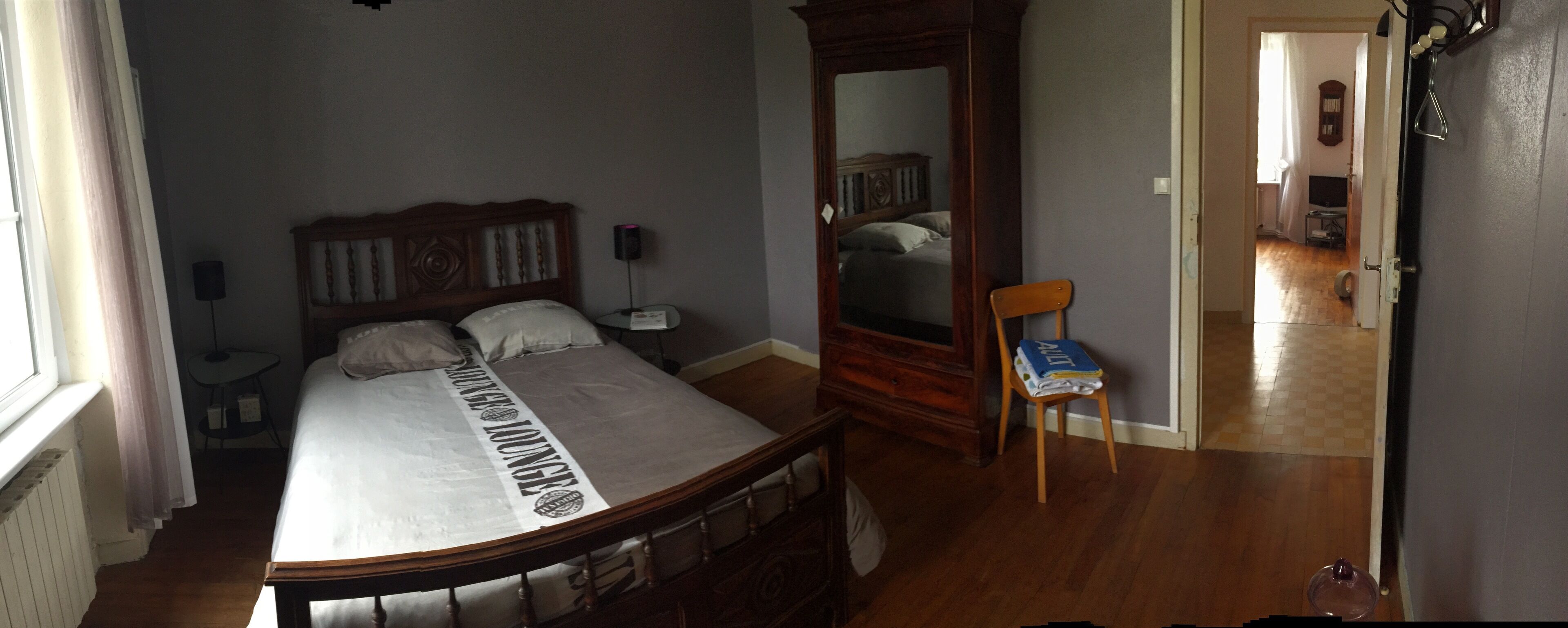 A bedroom with a wooden bed, a bedside table, a mirror, and a chair.