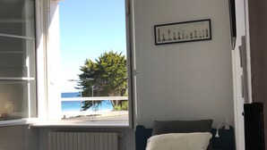 Un dormitorio con una cama, un ventanal con vistas al mar, un radiador y un cuadro en la pared.
