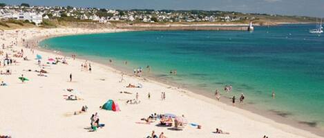 Une plage bondée où les gens se prélassent au soleil et se baignent.