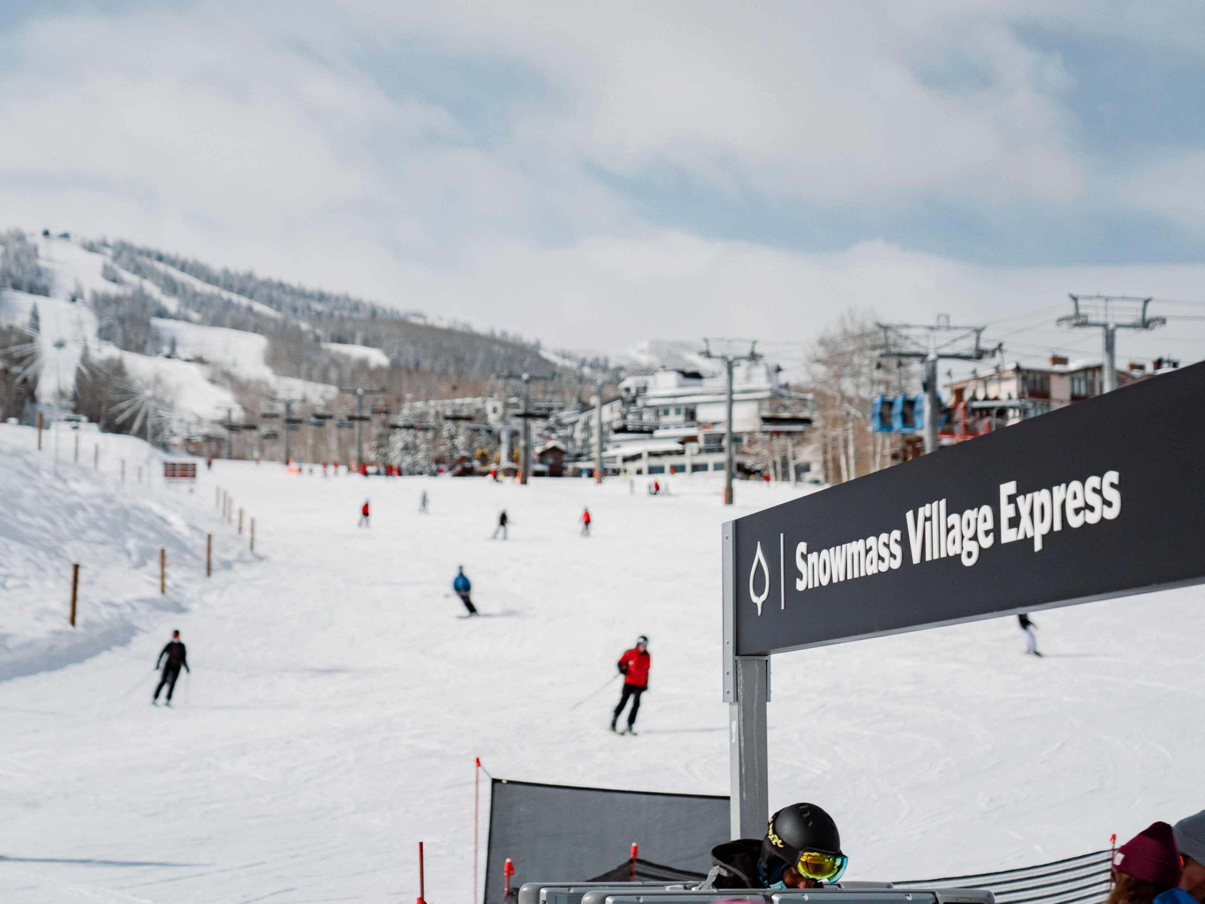 Señal del Snowmass Village Express con una pista de esquí al fondo.