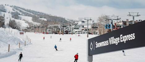 Señal del Snowmass Village Express con una pista de esquí al fondo.
