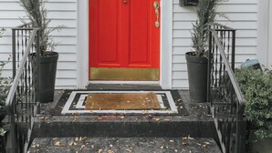Una puerta roja con un toldo blanco y negro, un buzón y una placa con un número.