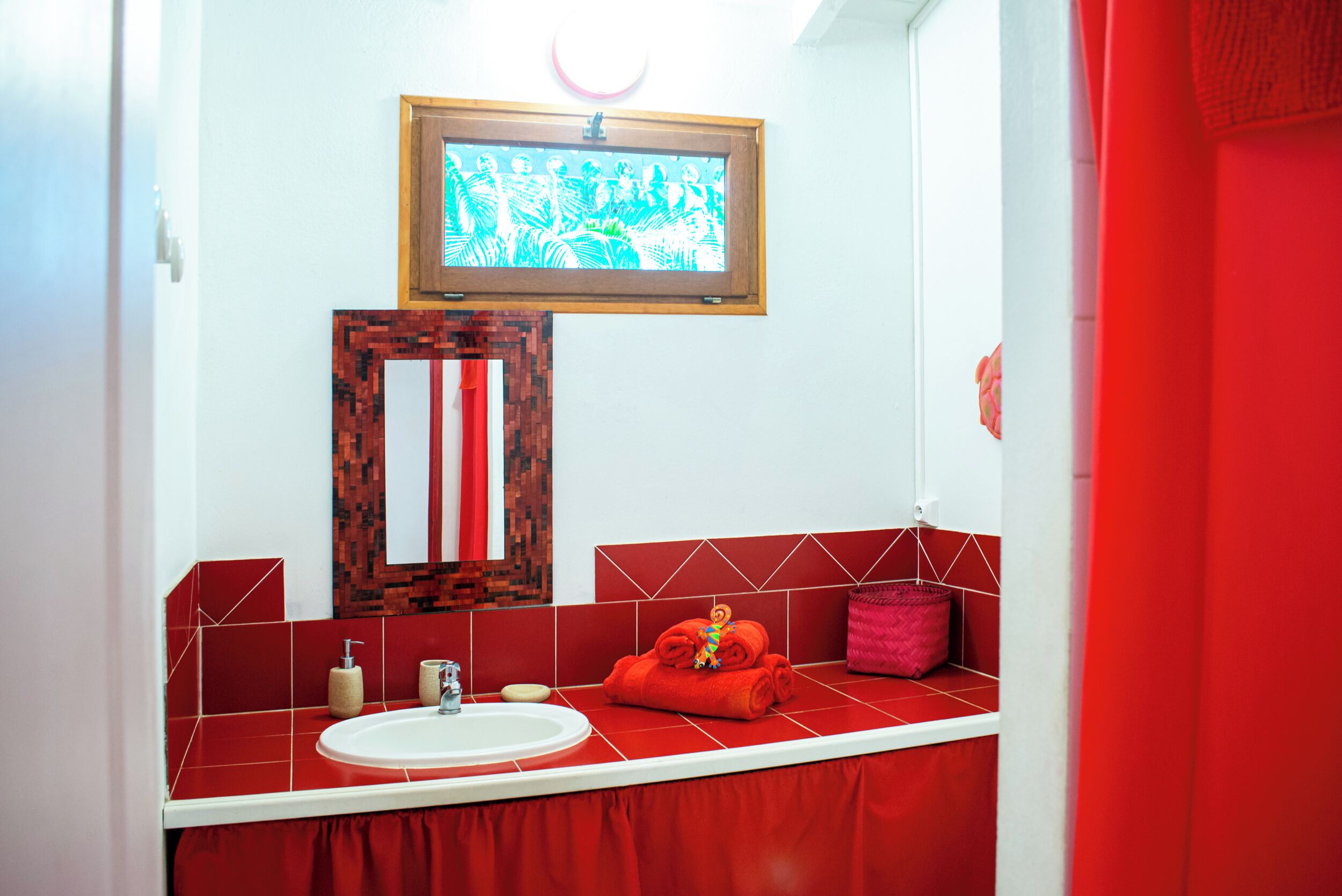 Une salle de bain avec des carreaux rouges, un lavabo blanc, un miroir et une serviette rouge posée sur le comptoir.